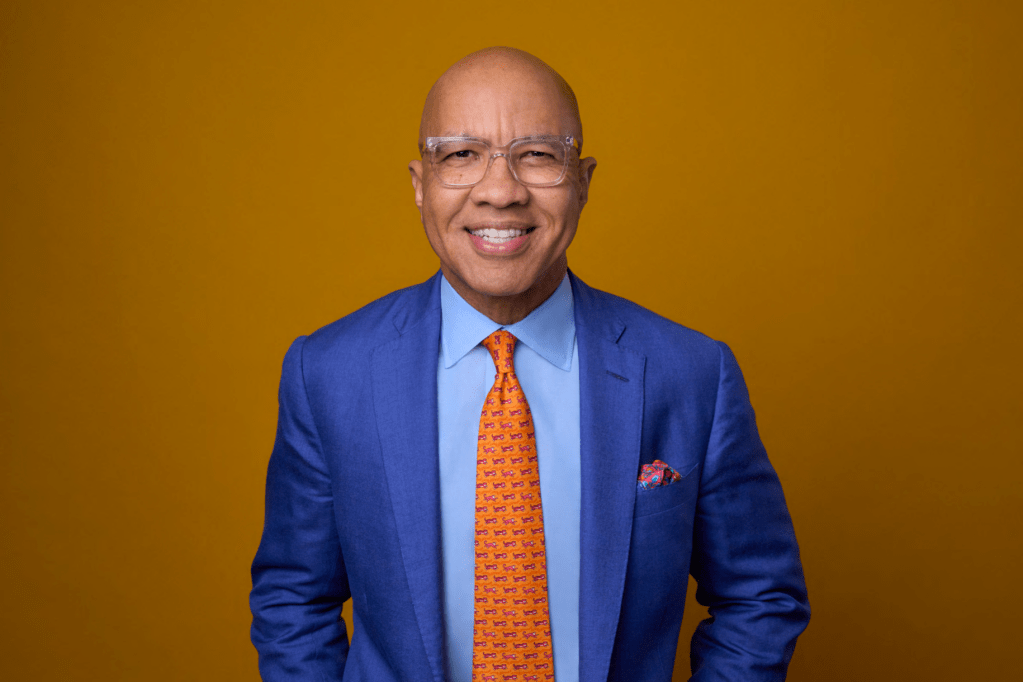 Man in a suit smiling with a yellow background.