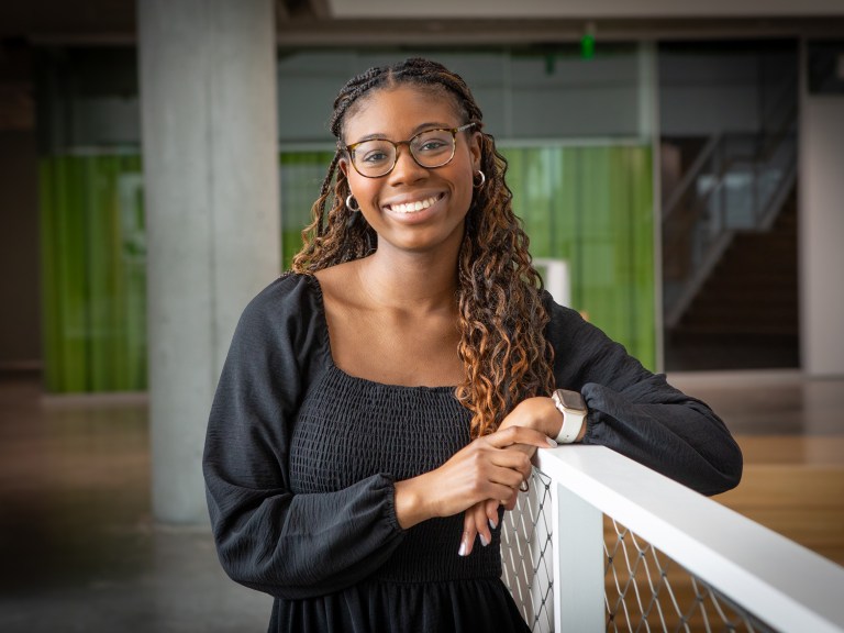 A graduating student leans against a white railing.