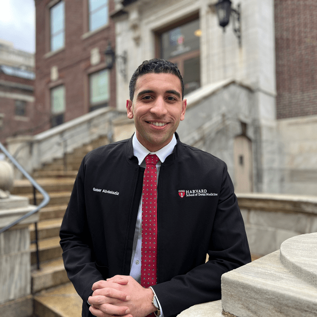 A student wearing a black jacket poses in front of the Harvard School of Dental Medicine entrance.