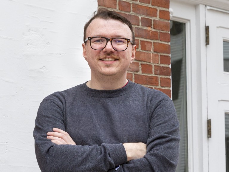 A man with glasses standing next to a brick wall