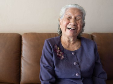 An older person smiling on a couch