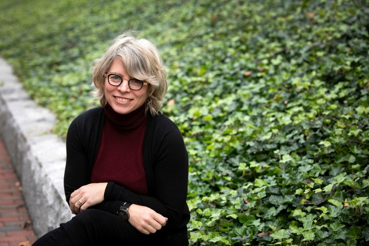A woman sits on a stone wall by a grassy area.